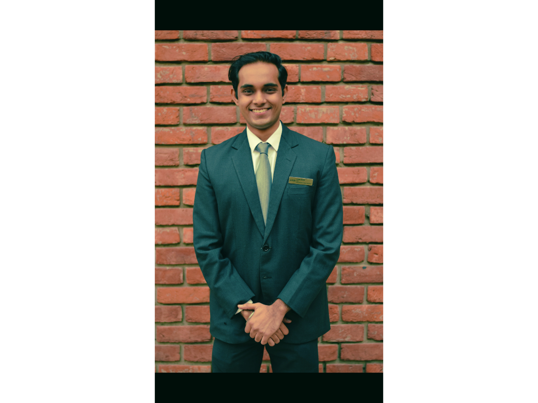 Ishan Basak smiling in formal attire against a brick wall